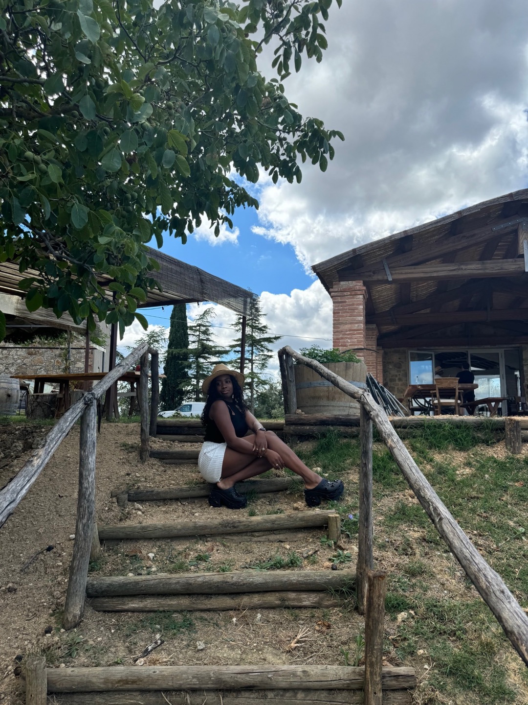 Rashana seated on rustic wooden steps in the Tuscan countryside